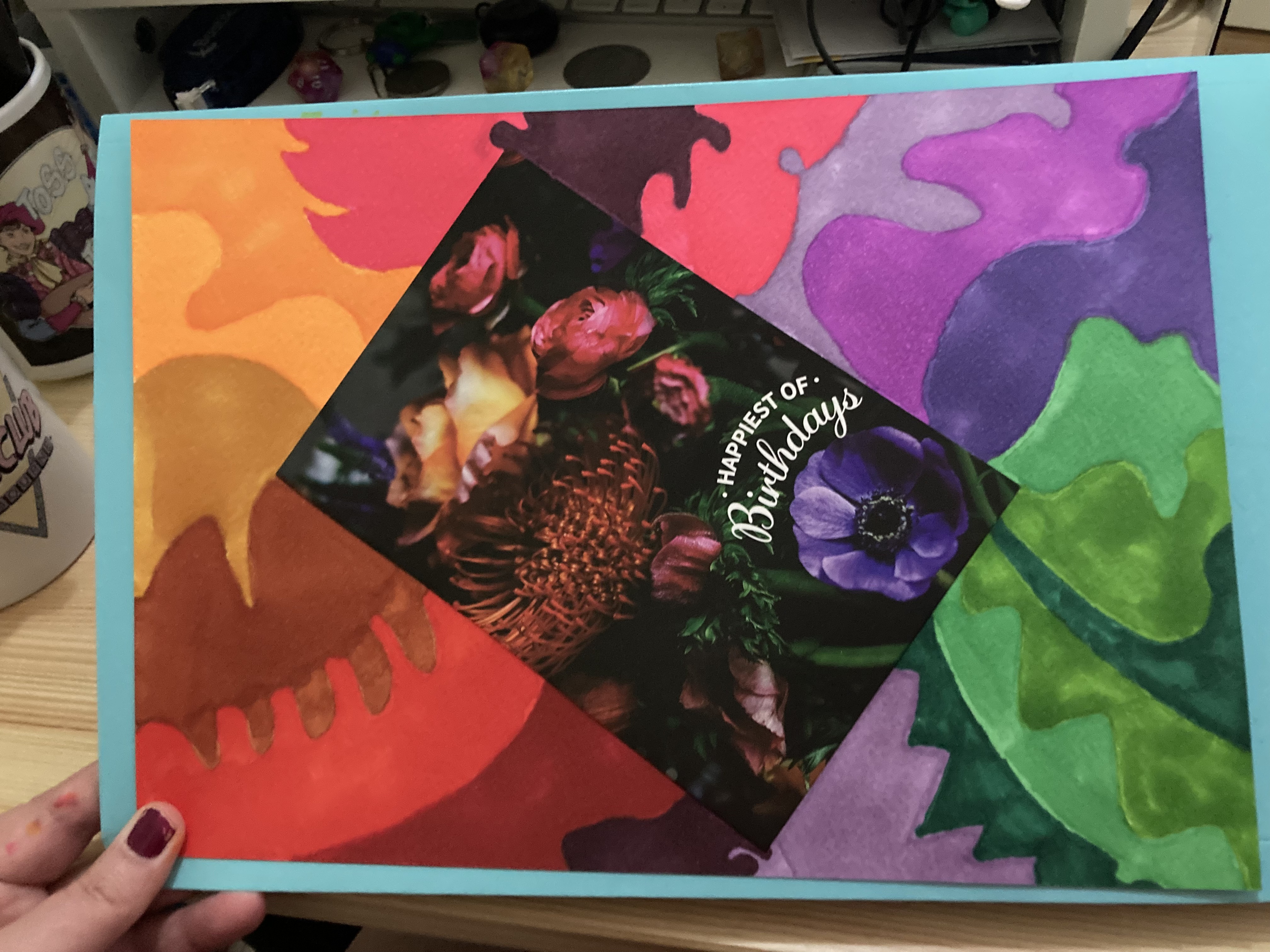 A floral birthday card is stuck on the paper at an angle and markers have been used to make it look like the colours of the card are flowing out onto the page.